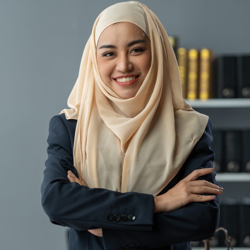 An Asian Muslim female lawyer wearing a hijab stands with her arms crossed. Confident smiling at wor